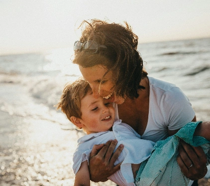A mother holding a smiling young child in her arms on a sunny beech