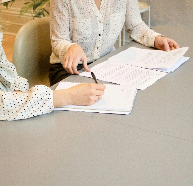 Two people sitting at a desk reviewing documents and taking notes