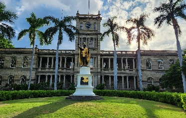 statue of a king in front of building with palm trees